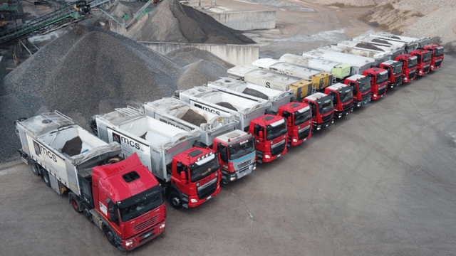 Fleet of MCS automated silo trucks lined up at a construction materials production site.