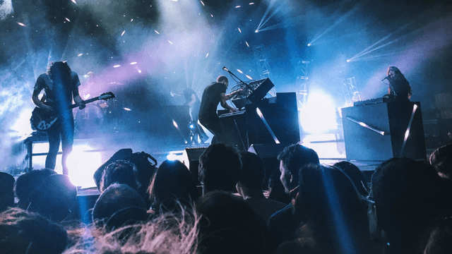 Live rock concert with musicians performing onstage under blue lights before a large audience.