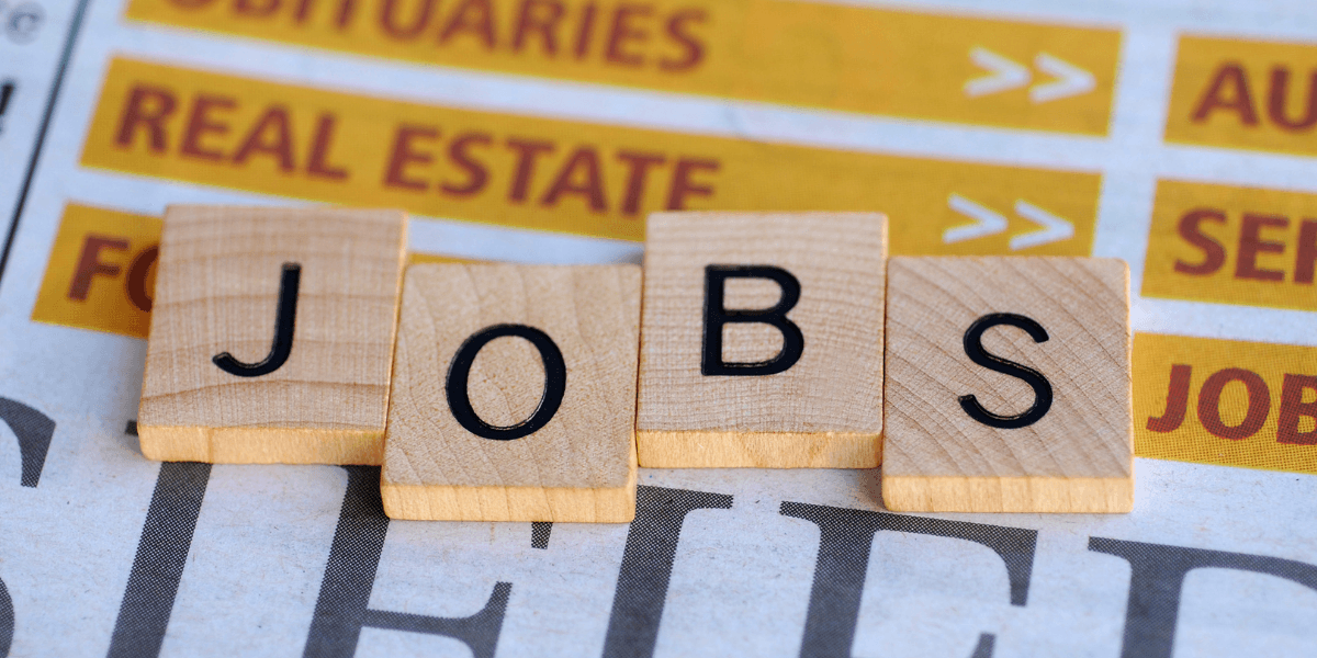 Wooden letter tiles spelling "JOBS" on a newspaper background featuring job listings