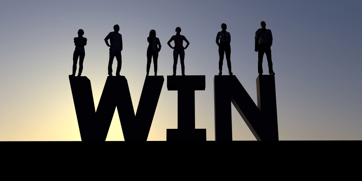 Silhouetted figures stand on large letters spelling "WIN" against a sunset backdrop