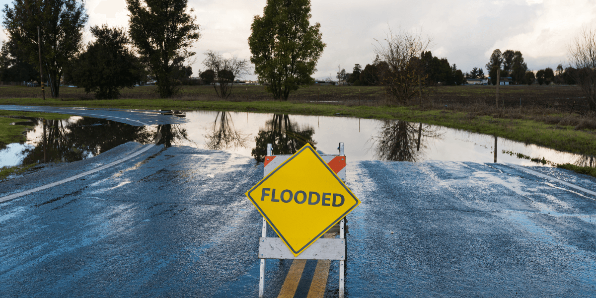 Flooded road sign on a wet, water-logged street with reflections in puddles
