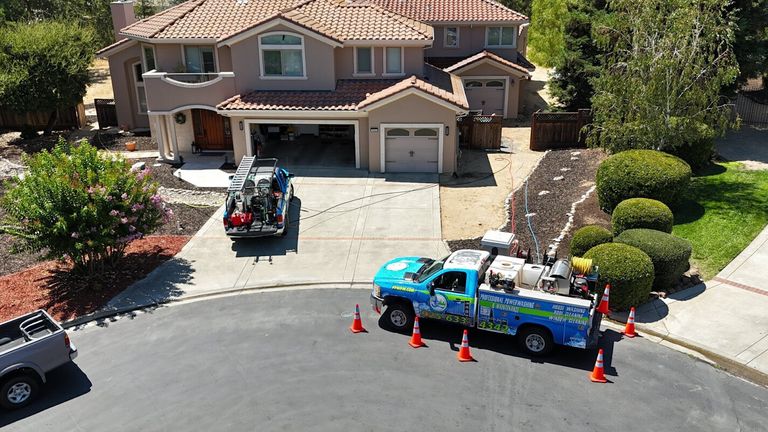 Blue truck with power washing equipment parked outside a residential property, surrounded by traffic cones.