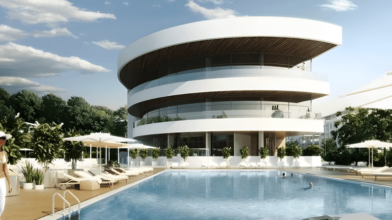 Modern circular luxury building overlooking resort-style pool with loungers, umbrellas, and woman walking along deck.
