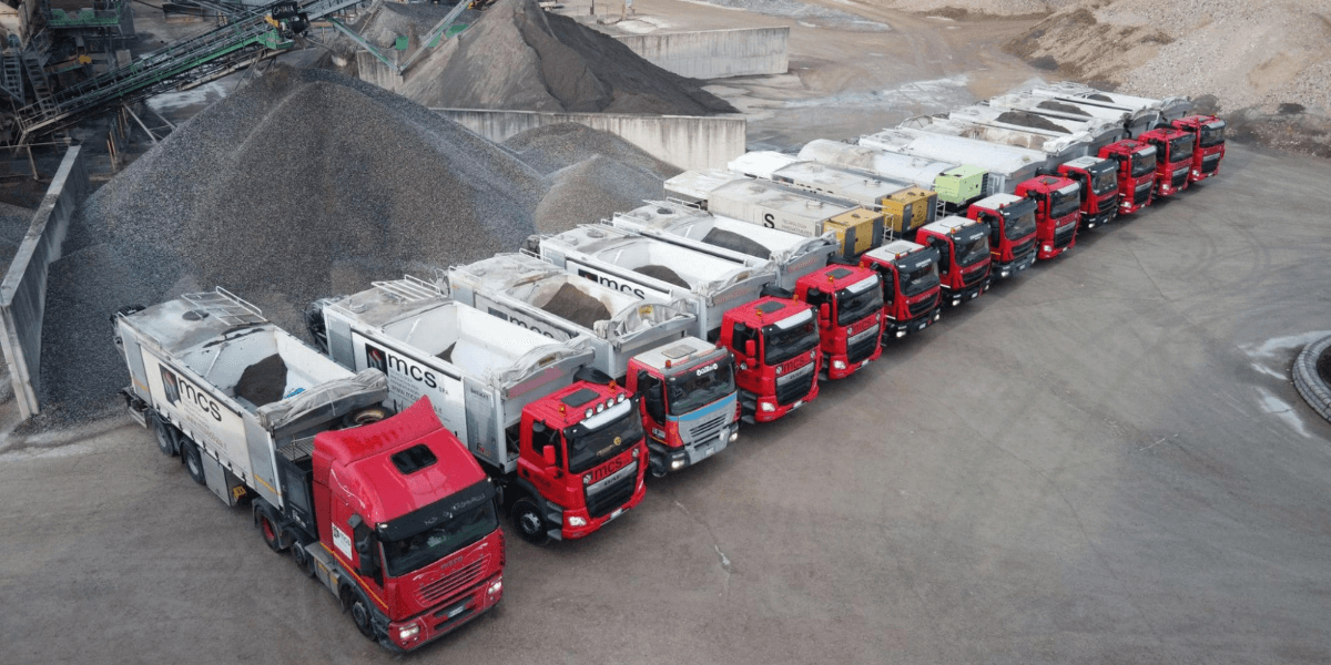 Fleet of MCS automated silo trucks lined up at a construction materials production site.