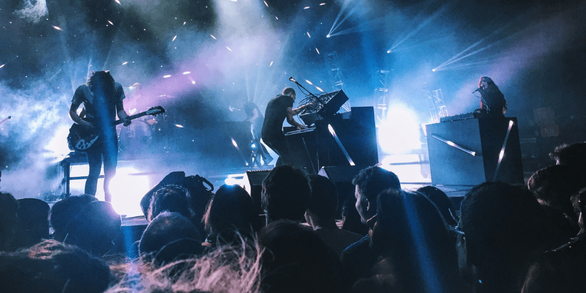 Live rock concert with musicians performing onstage under blue lights before a large audience.