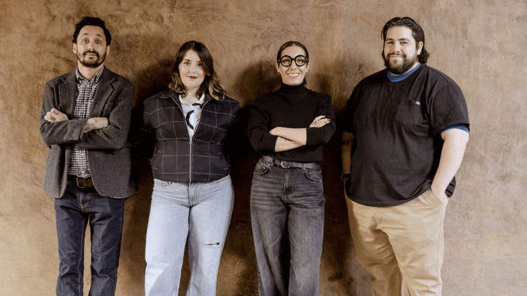Four team members of ATRIUM Creative Agency standing together against a textured brown wall, smiling confidently.