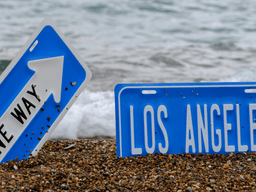 Two blue road signs on a sandy beach with ocean waves in the background
