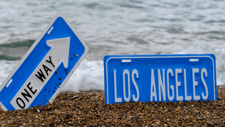 Two blue road signs on a sandy beach with ocean waves in the background