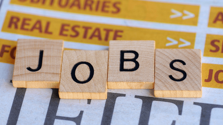 Wooden letter tiles spelling "JOBS" on a newspaper background featuring job listings