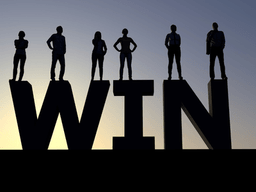 Silhouetted figures stand on large letters spelling "WIN" against a sunset backdrop