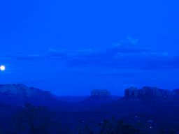 Nighttime landscape featuring mountains under a full moon and a deep blue sky