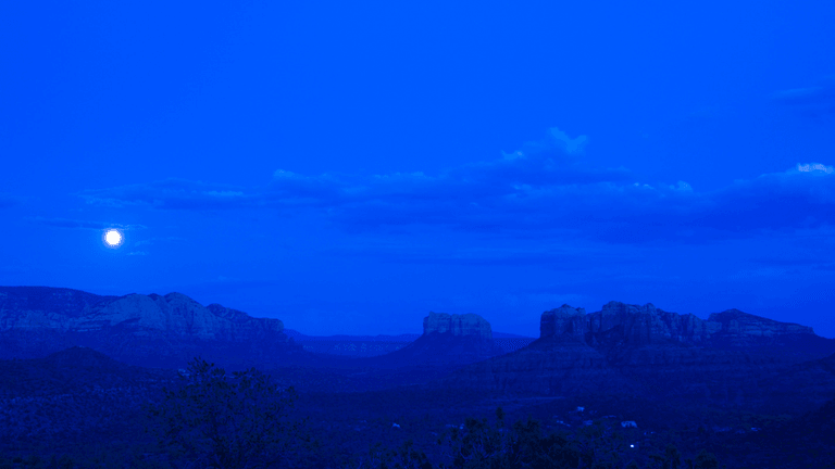 Nighttime landscape featuring mountains under a full moon and a deep blue sky