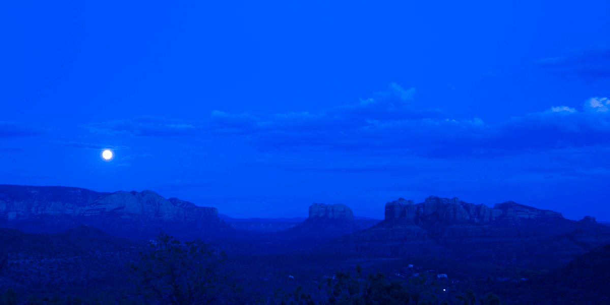 Nighttime landscape featuring mountains under a full moon and a deep blue sky