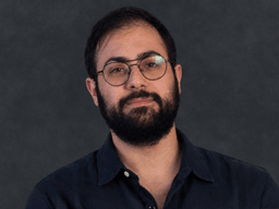 A man with glasses and a beard poses confidently against a dark background
