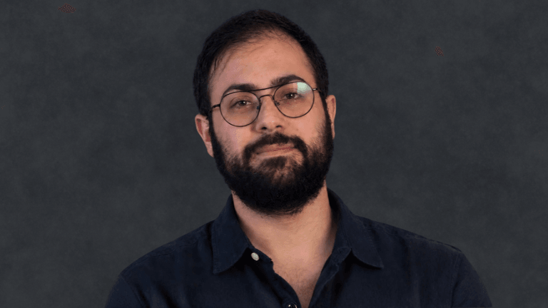 A man with glasses and a beard poses confidently against a dark background