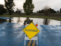 Flooded road sign on a wet, water-logged street with reflections in puddles