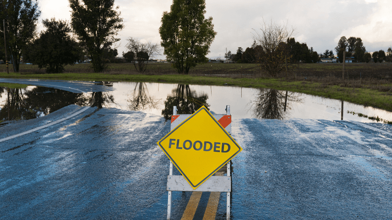 Flooded road sign on a wet, water-logged street with reflections in puddles