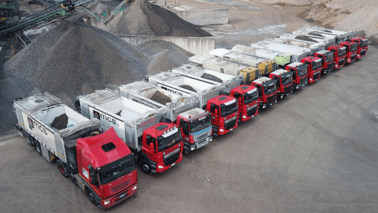 Fleet of MCS automated silo trucks lined up at a construction materials production site.