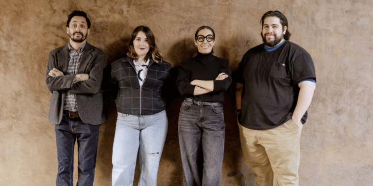 Four team members of ATRIUM Creative Agency standing together against a textured brown wall, smiling confidently.