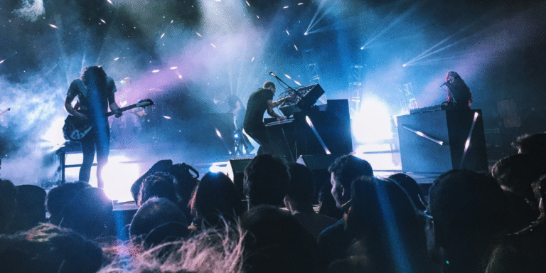 Live rock concert with musicians performing onstage under blue lights before a large audience.