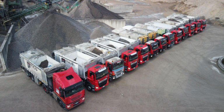 Fleet of MCS automated silo trucks lined up at a construction materials production site.